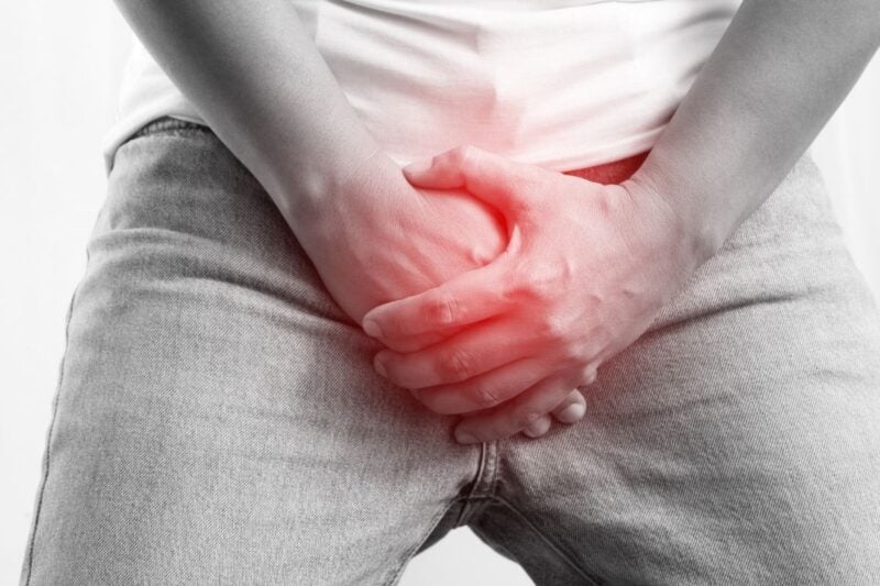 Man in faded jeans with hands highlighted in red covering groin depicting painful ejaculation