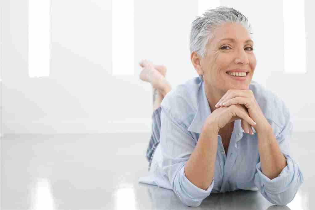Gray haired senior in white shirt lying on her stomach with a broad smile