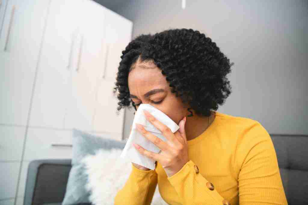 Young lady with allergies and white tissues held to her face while blowing her nose. 