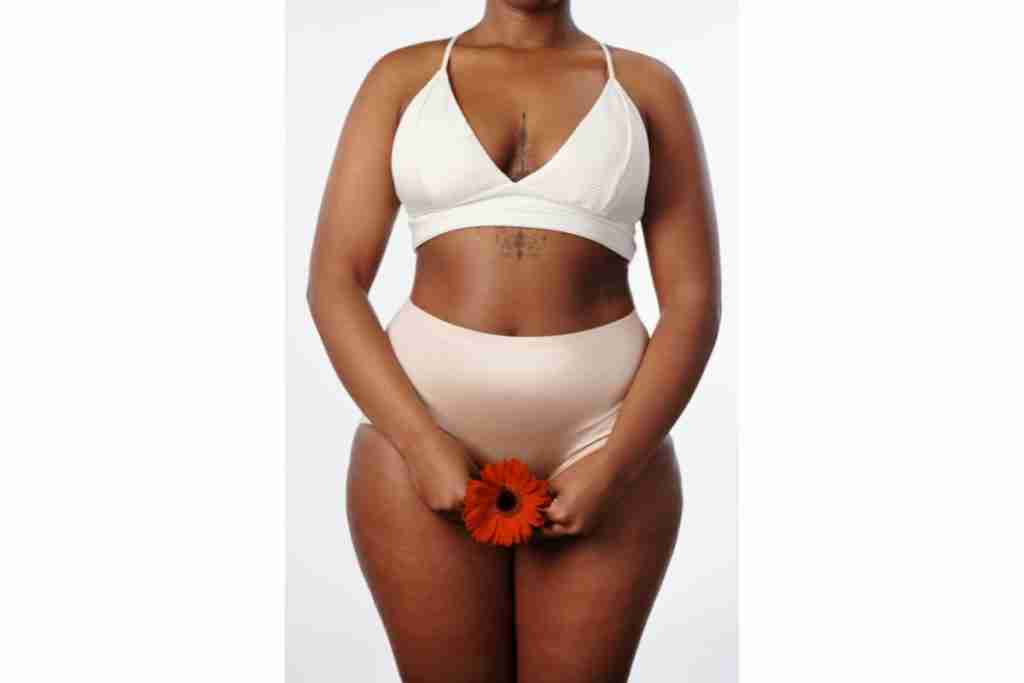 African lady in white bra and pants holding a red flower in front of her vagina