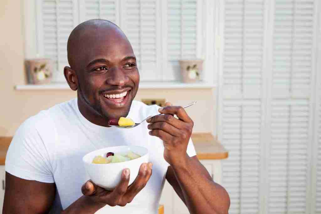 Black man smiling as he east a bowl of healthy food bought on his budget plan