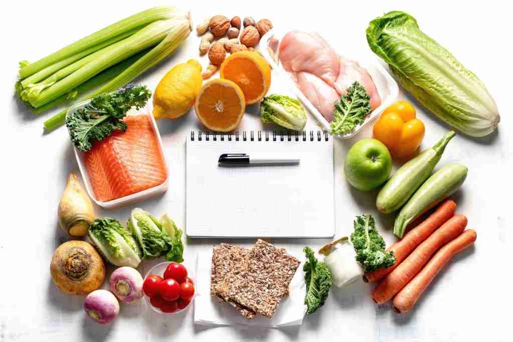 Photo of different healthy foods with a notepad and pen for making a list 