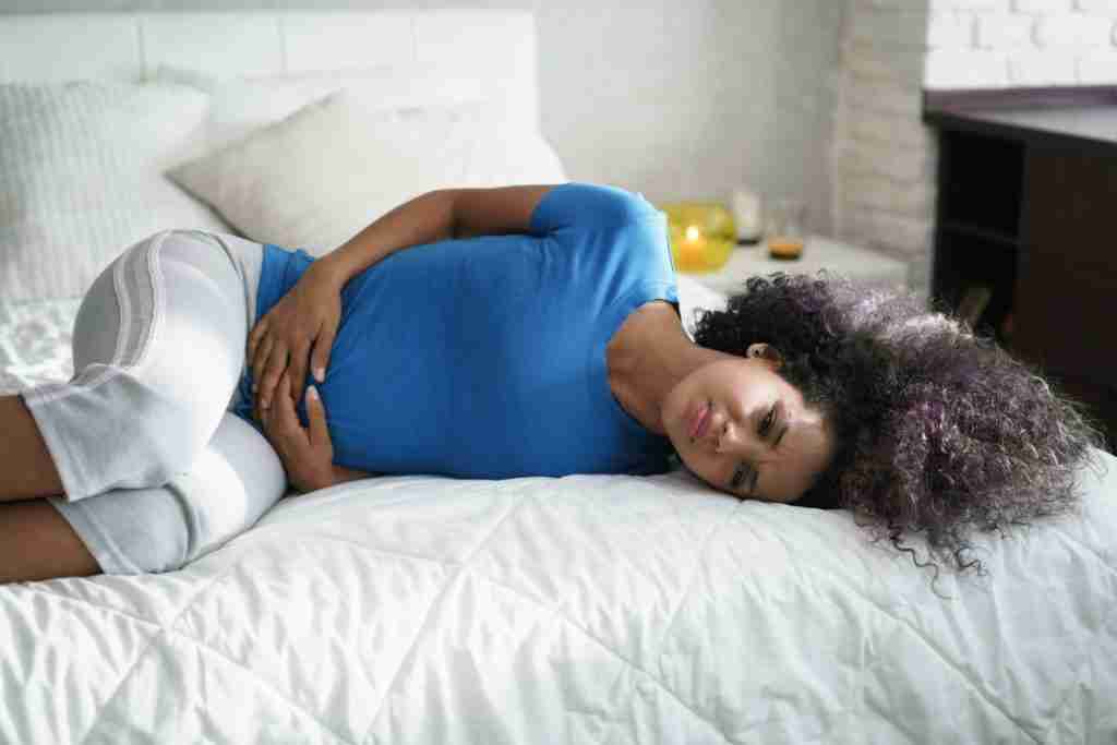 Black lady lying in bed with pelvic cramps -this is when to worry about your fibroid symptoms