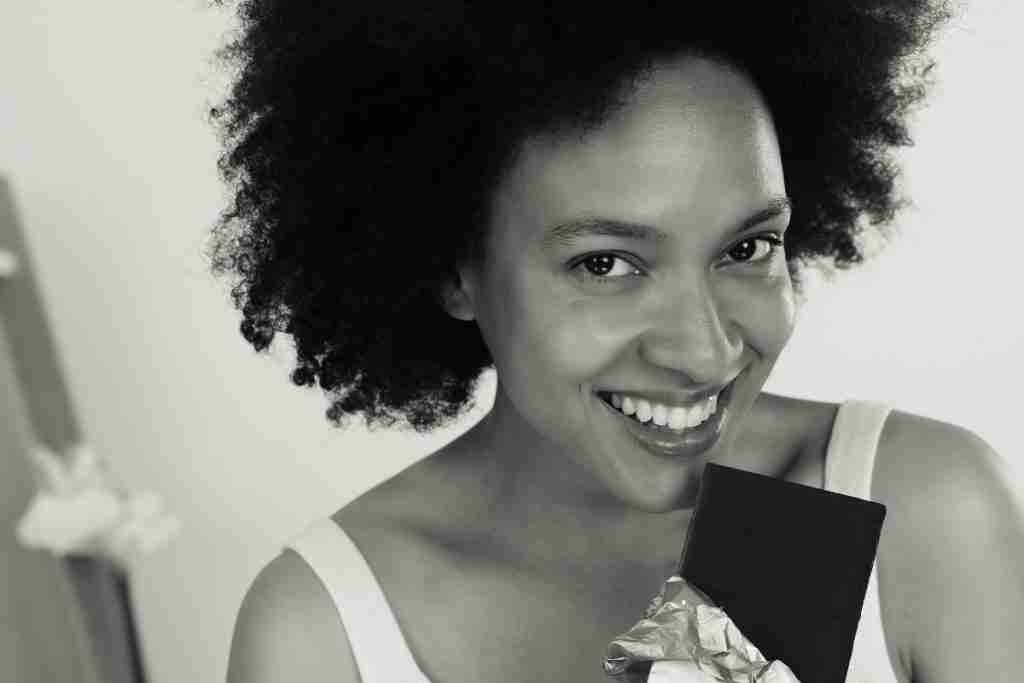 Black and white image of African lady with afro enjoying a piece of dark chocolate and its health benefits