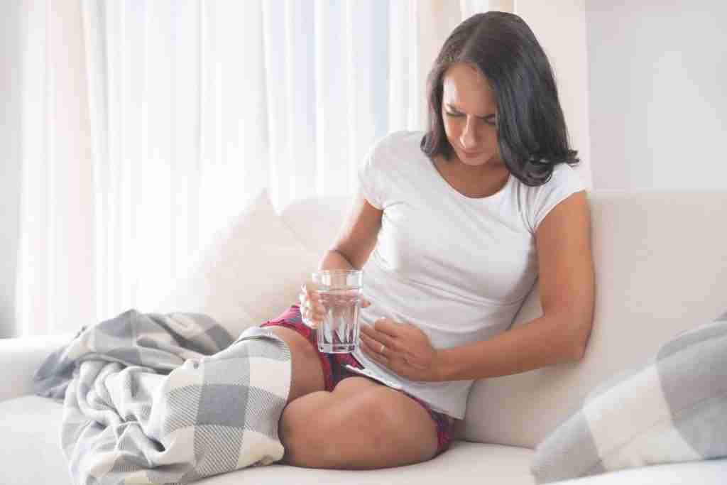 Woman in pain from stomach ulcer holding a glass of water