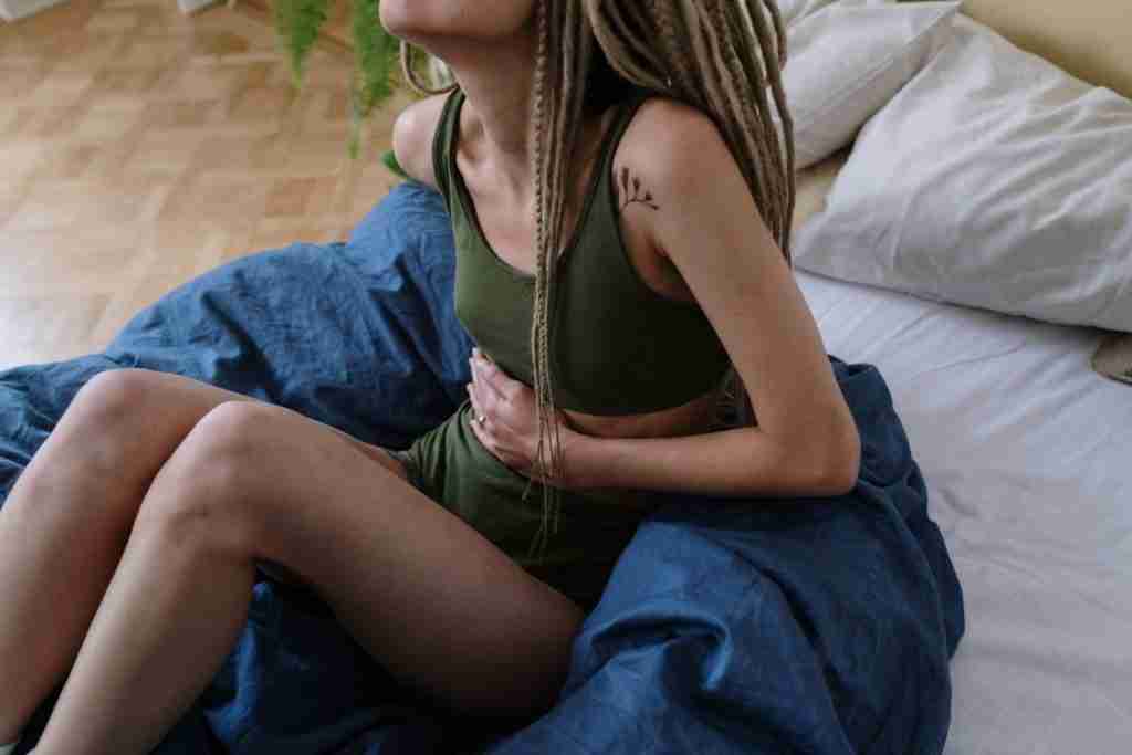 Tiredness and feeling unwell can be symptoms of fatty liver, lady sitting up on bed feeling unwell