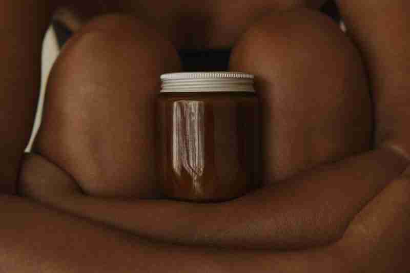 Lovely chocolate-skinned lady with arms folded under a brown jar of cream between her knees