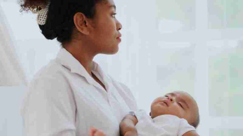 New mum holding her baby as she looks out of the window and contemplates going home to continue her CS recovery