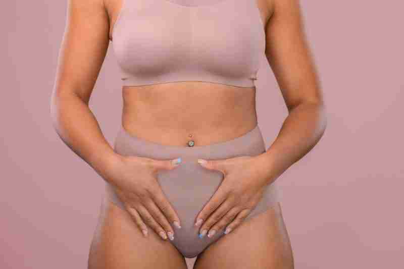 Woman in beige underwear, with both hands placed over her pelvic indicating gynaecological conditions which have similarities and differences such as PCOS vs. Endometriosis