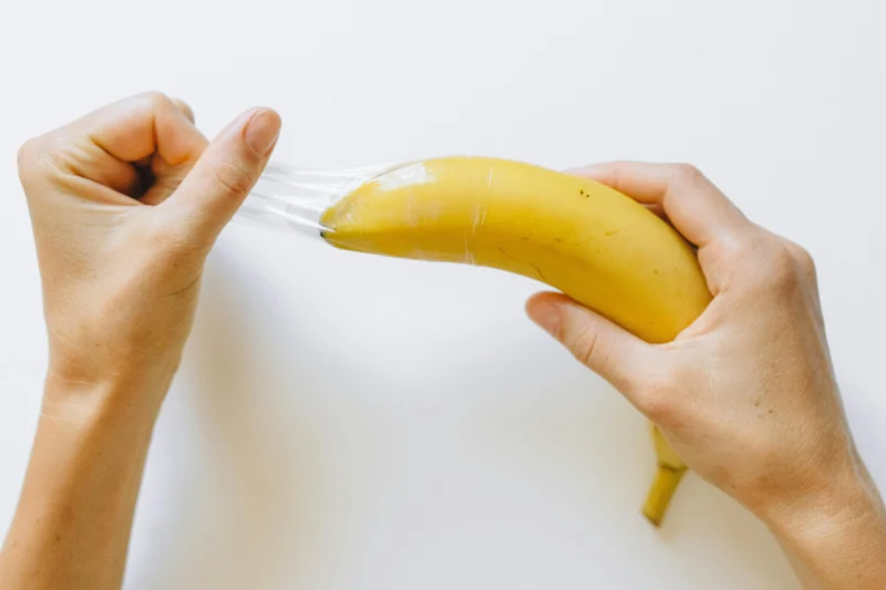 Hands demonstrating how to put a condom on a banana, commonly used as a safe sex education visual aid.