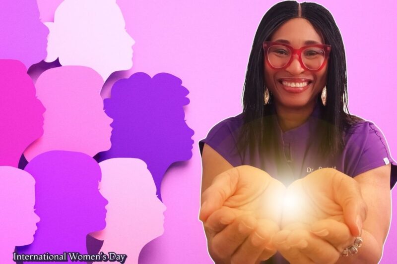 Askawayhealth founder Dr Sylvia International Womens Day 2026 Black woman in red glasses and purple scrubs smiling while holding a glowing ball reflecting the IWD theme Give to Gain
